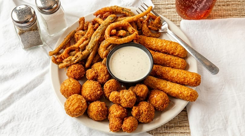 A platter of fried appetizers including green beans, onion rings, mozzarella sticks, and hushpuppies with ranch.
