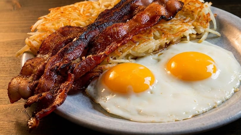A breakfast plate with crispy bacon, golden hash browns, and two sunny-side-up eggs.