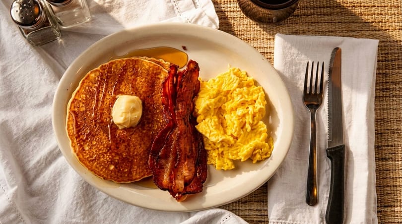 A breakfast plate with pancakes, bacon, and scrambled eggs, with salt and pepper shakers nearby.